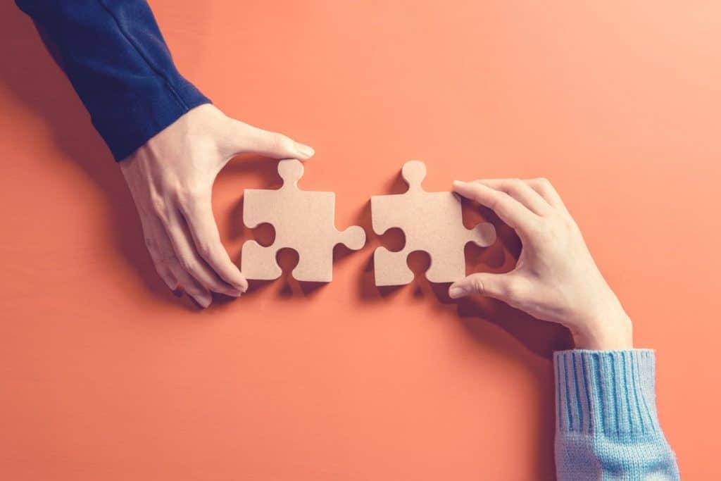 two hands pushing puzzle pieces together